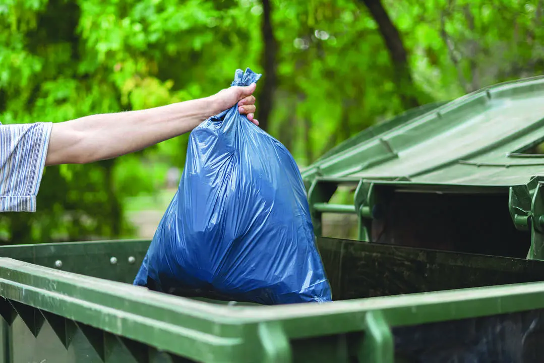 male dumping waste package into a big trash bin container