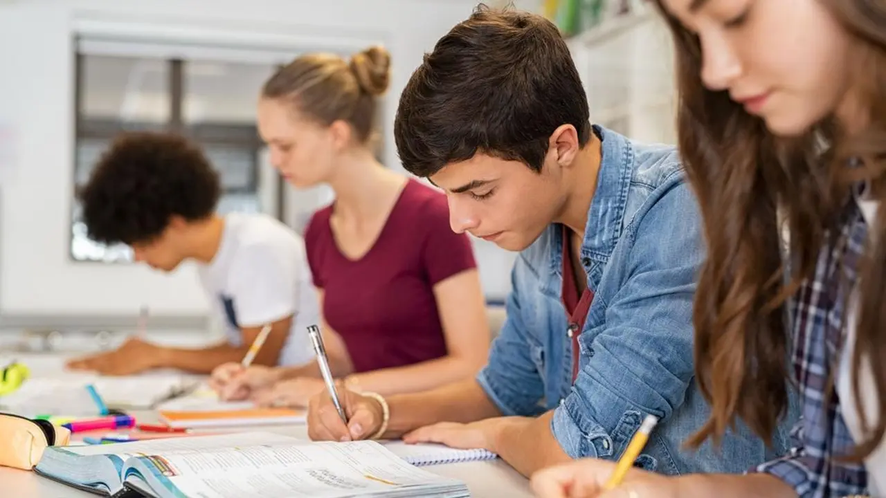 Group of college students studying in classroom writing notes during lesson. Focused guy and girls studying in college library sitting at desk. Group of multiethnic university students doing research sitting in a row.