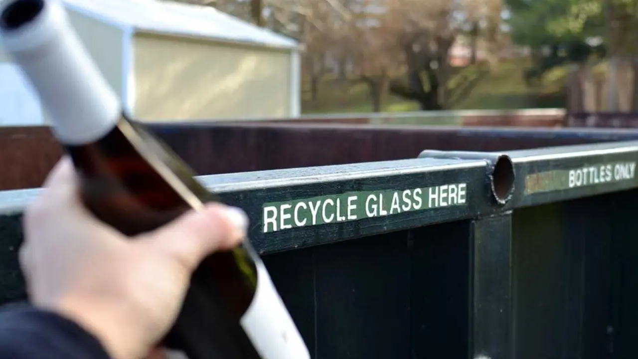 Una persona lleva una botella de vidrio vac&iacute;a al contenedor para su reciclaje