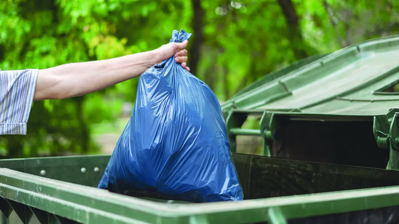 male dumping waste package into a big trash bin container