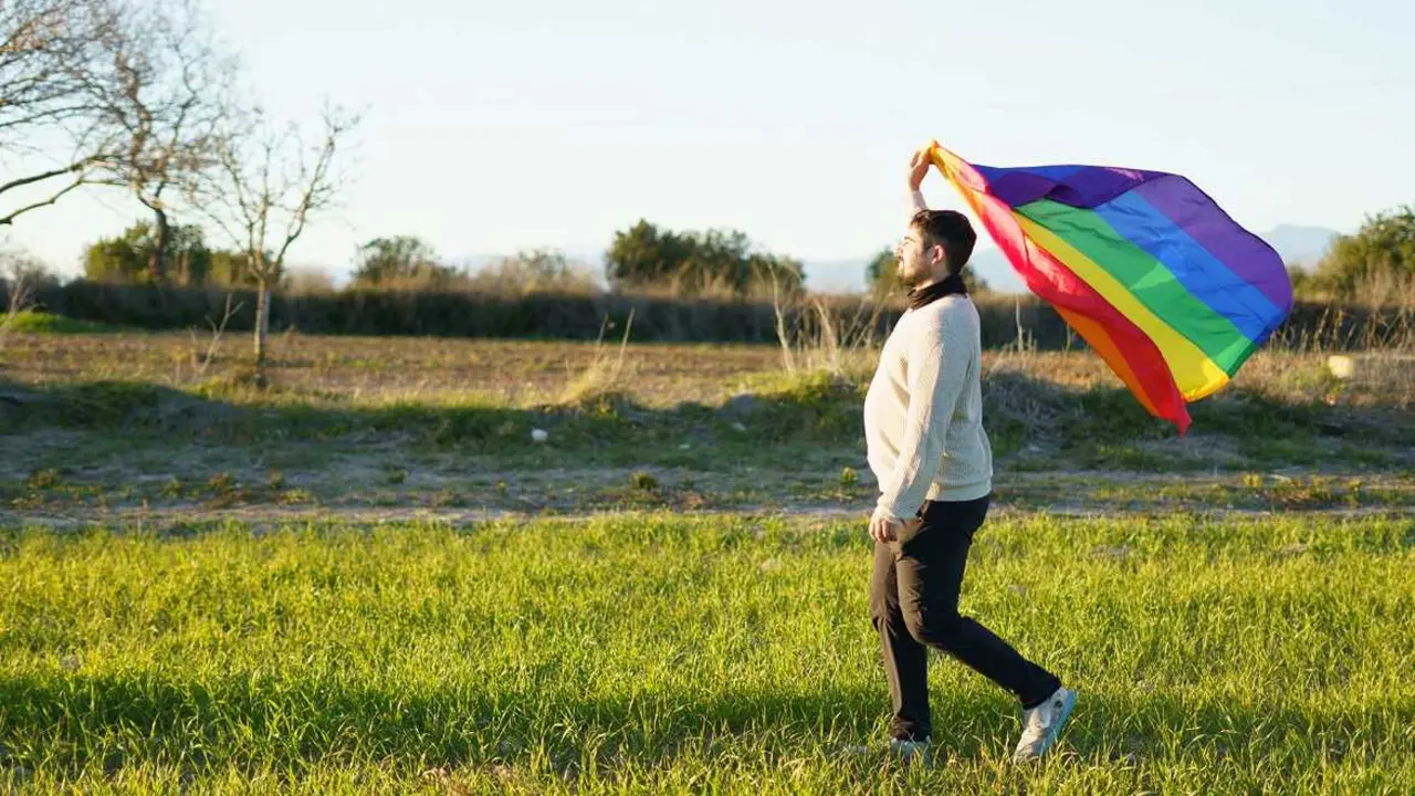 Un hombre con una bandera LGTBI en el campo